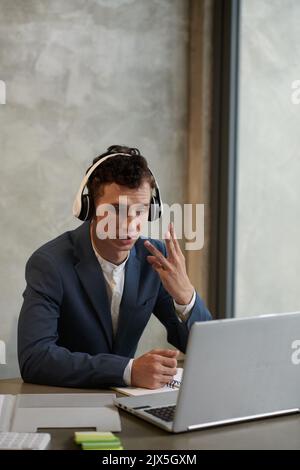 Young businessman showing tree fingers when talking to colleague during online meeting Stock Photo