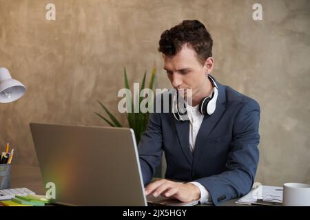 Serious frowning businessman working on laptop, filling documents and answering e-mails Stock Photo