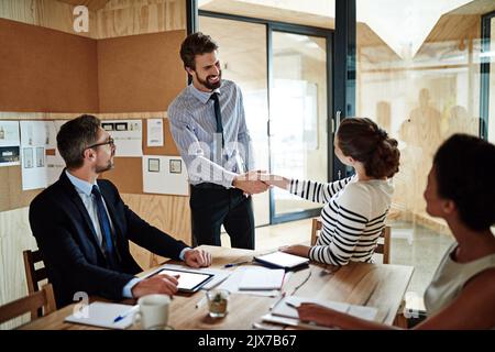 Making new business aquaintances. two colleagues shaking hands together in an office while colleagues look on. Stock Photo