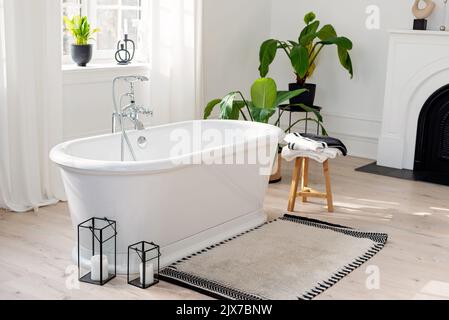 Stylish modern bathroom interior. Horizontal view of an empty free-standing bathtub on a wooden floor in a bright room against the backdrop of a large Stock Photo