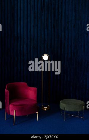Apartment with comfortable red velour armchair, minimalist floor lamp and green pouf or ottoman in living room with dark blue velvet wall panels and f Stock Photo