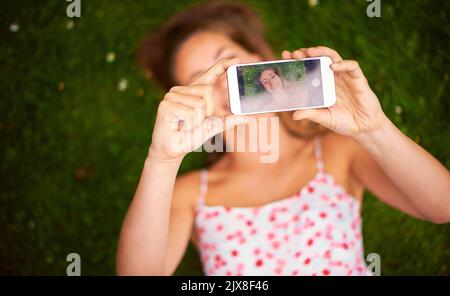 Taking a summer selfie to share with her friends. a young woman taking a selfie while lying on the grass. Stock Photo