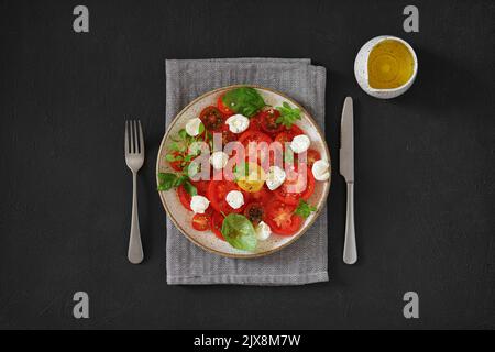 Summer fresh diet salad with tomatoes, mozzarella cheese, basil and olive oil on dark background. Healthy lunch, bright salat. Stock Photo
