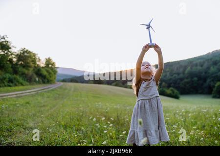 Little girl standing in nature with model of wind turbine. Concept of ecology future and renewable resources. Stock Photo