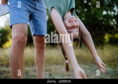 Father swing her daughter, holding her upside down, having fun together in nature. Stock Photo