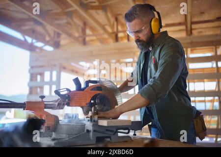 Construction worker working with eletric saw inside wooden construction of house, diy eco-friendly homes concept. Stock Photo