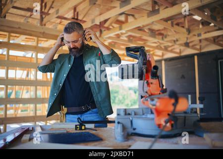 Construction worker working with eletric saw inside wooden construction of house, diy eco-friendly homes concept. Stock Photo