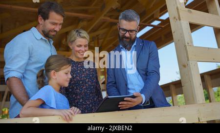 Sales Agent showing plans of new house to young family on construction site. Stock Photo