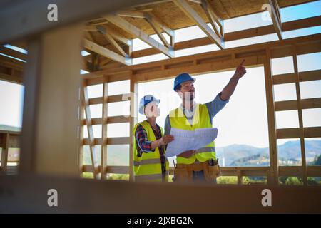 Construction engineers or architects with blueprints visiting and chcecking eco building site of wood frame house Stock Photo