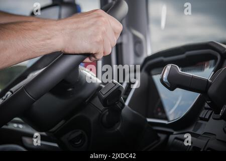 Closeup Side View Photo of Dashboard in the Truck with Caucasian Driver’s Hands on Steering Wheel. Heavy Duty Transportation Theme. Stock Photo