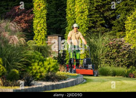 Large and Beautiful Landscape Garden in the Backyard of Residential House. Professional Landscaper in Protective Headphones Taking Care of Design Appe Stock Photo