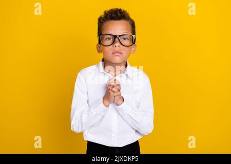 Portrait of sad boy hand hold together ask help homework exercise test isolated on yellow color background Stock Photo