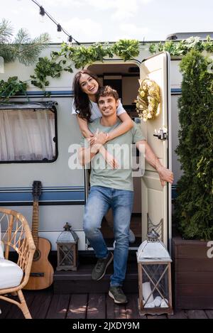 Smiling couple hugging and looking at camera near door of camper van outdoors,stock image Stock Photo