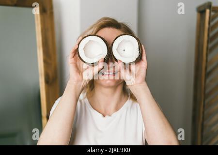 A beautiful girl holds halves of a coconut in her hands and covers her eyes with them Stock Photo