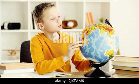 schoolboy in yellow jumper looking at globe near notebook and books on desk,stock image Stock Photo