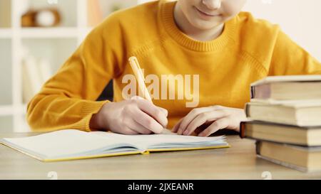 cropped view of pleased schoolkid writing in notebook while doing homework near books on wooden desk,stock image Stock Photo