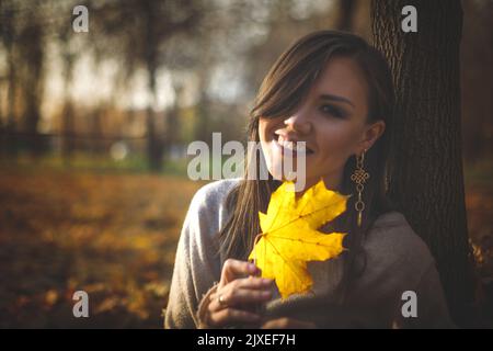 Portrait of a young Central Asian woman with a yellow maple leaf in her hands in the evening autumn park Stock Photo