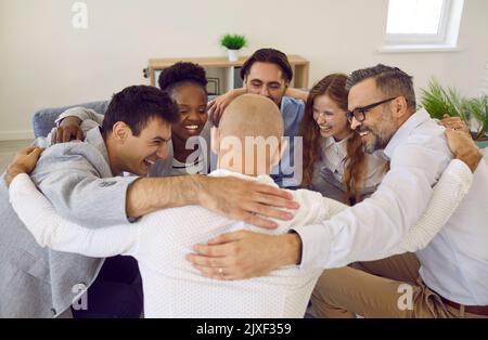 Team of successful positive colleagues laughing and hugging while standing in circle in office. Stock Photo