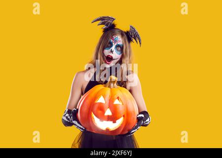 Girl in Halloween costume holding Jack o lantern and looking at camera with surprised expression Stock Photo