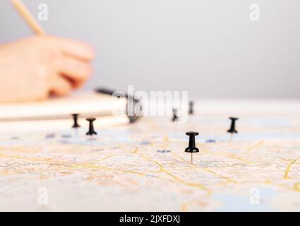 Woman planning travel itinerary. Hand taking notes in planner and marking locations to visit on map with pins. Trip route organization. High quality p