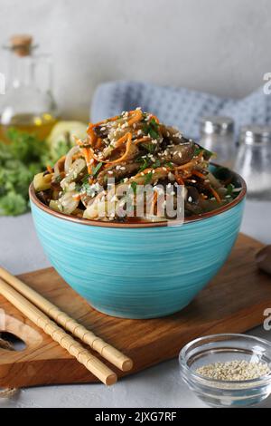 Korean eggplant salad with sesame seeds, onions and carrots in blue bowl on wooden board Stock Photo