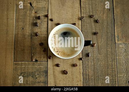 wooden table with close-up on coffee cup and coffee beans in shape of heart Stock Photo