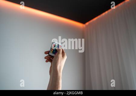 Hand holding led lighting remote control with light turned on ceiling Stock Photo