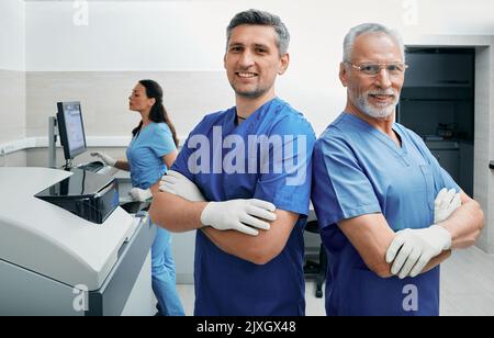 Laboratory technicians standing against backdrop of medical lab while female assistant working with laboratory equipment Stock Photo