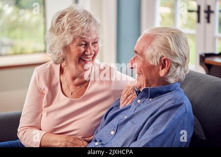 Loving Senior Couple Enjoying Retirement Sitting On Sofa At Home Talking And Laughing Together Stock Photo