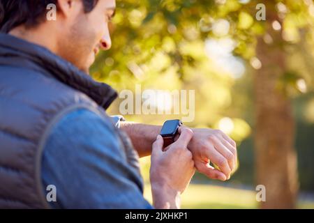 Mature Man Standing By Trees In Autumn Park Looking At Smart Watch Stock Photo