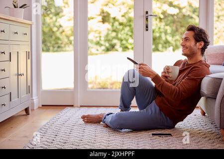 Man At Home Sitting On Floor With Remote Control Watching TV Stock Photo