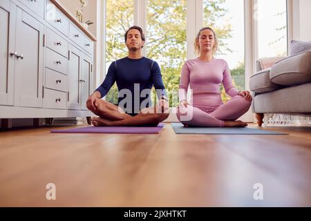 Couple Sitting On Mats At Home Doing Yoga Exercises Together Stock Photo
