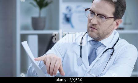 serious cardiologist in glasses pointing with finger at cardiogram in hospital,stock image Stock Photo