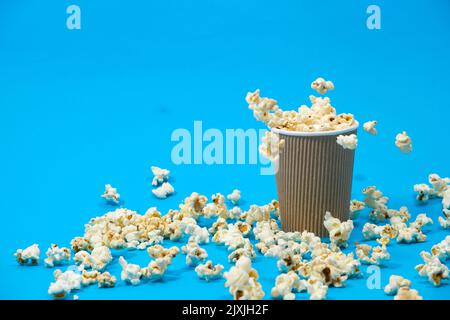 Popcorn is poured into a paper brown glass on a blue background with place for text. Stock Photo