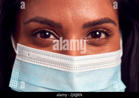 Close Up Portrait Of Female Mature Woman Wearing Face Mask In Front Of Blue Studio Background Stock Photo