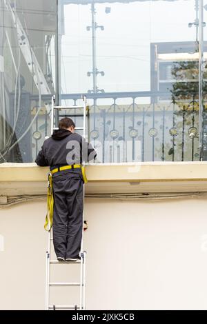 An electrician on ladder performs work. Worker in work clothes on stairs Stock Photo