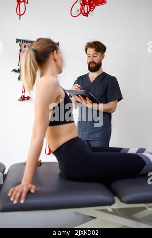 Rhabilitologist doctor taking notes on his clipboard of the history of his female patient who is lying on the couch Stock Photo