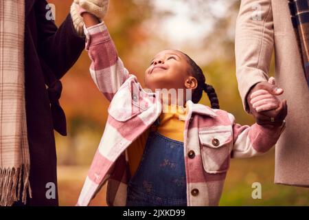Close Up Of Mother And Father Holding Hands With Daughter On Walk Through Autumn Countryside Stock Photo