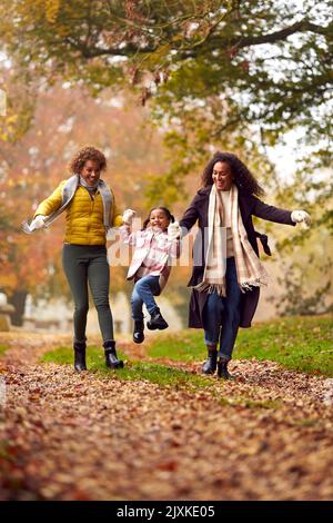 Multi-Generation Female Family Swinging Granddaughter On Walk Through Autumn Countryside Together Stock Photo