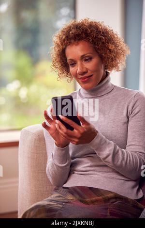 Senior Woman Sitting On Sofa At Home Using Mobile Phone Stock Photo