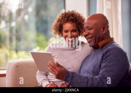 Senior Couple Sitting On Sofa At Home Using Digital Tablet Watching Streaming Movie Together Stock Photo