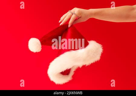 Close Up Studio Shot Of Woman Holding Christmas Santa Hat Against Red Background Stock Photo