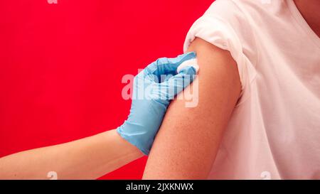 Studio Shot Of Woman Having Arm Swabbed Before Injection Or Vaccination Against Red Background Stock Photo
