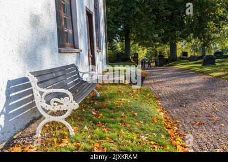 Park bench by a church and fallen autumn leaves Stock Photo