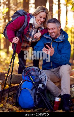 Mature Retired Couple Walk In Fall Or Winter Countryside Using Map Or Navigation App On Mobile Phone Stock Photo