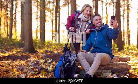 Mature Retired Couple Walk In Fall Or Winter Countryside Posing For Selfie On Mobile Phone Stock Photo
