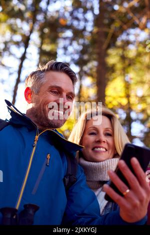 Mature Retired Couple Walk In Fall Or Winter Countryside Using Map Or Navigation App On Mobile Phone Stock Photo
