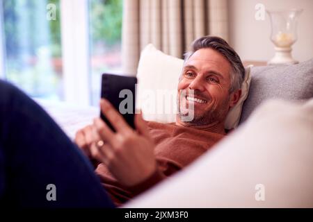 Mature Man At Home Relaxing On Sofa Using Mobile Phone For Texting Or Social Media Stock Photo
