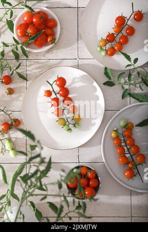 Fresh red cherry tomatoes on branch on white plates. Top view Stock Photo
