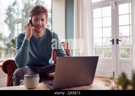 Man Working From Home Using Laptop And Mobile Phone Stock Photo